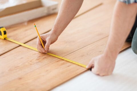 A person measuring a wooden floor with a ruler.